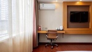A hotel room with a desk, chair, air conditioning unit, and a mounted television. - Companion Departure Hotel (Guangzhou)