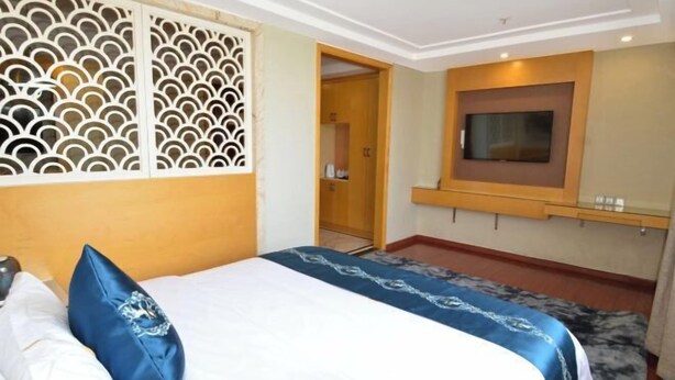 A bedroom with a bed, a TV mounted on the wall, and a wooden door leading to a bathroom. - Companion Departure Hotel (Guangzhou)