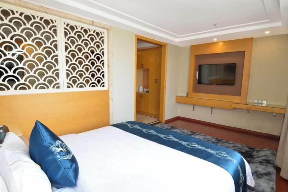 A bedroom with a bed, a TV mounted on the wall, and a wooden door leading to a bathroom.