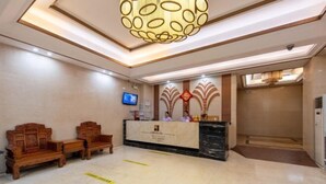 A hotel reception area with a reception desk, two wooden chairs, a television, and a modern chandelier. - Companion Departure Hotel (Guangzhou)