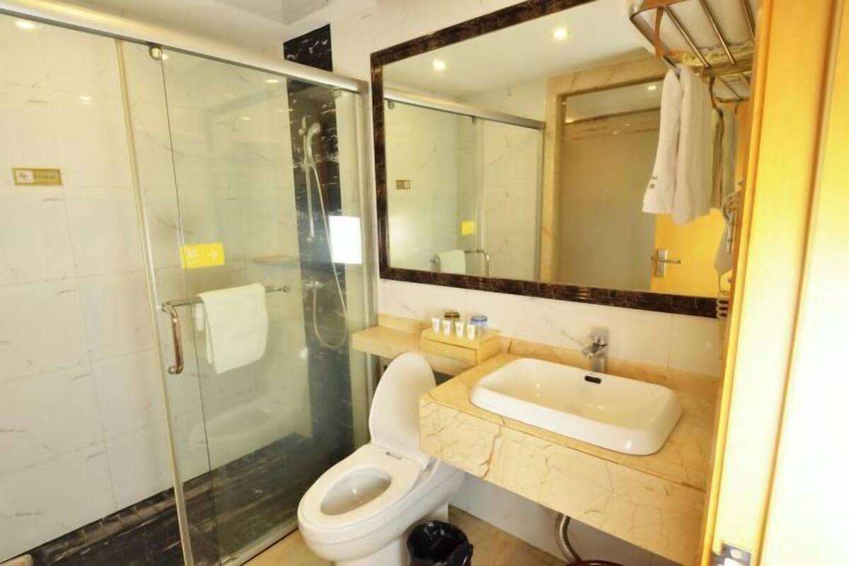 A bathroom with a glass shower enclosure, a toilet, a sink, and a mirror.