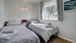 Une chambre avec deux lits, une fenêtre avec des rideaux, un tableau au mur et un luminaire au plafond.