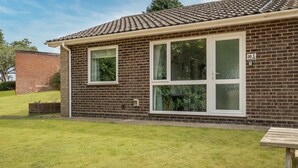 Une maison à deux étages, construite en briques, avec de grandes fenêtres et un petit jardin à l’avant.