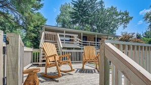 A wooden deck with rocking chairs and a table, a wooden staircase, and a building with a balcony. - Picturesque Phoenix Vacation Home on Oswego River! (Phoenix)