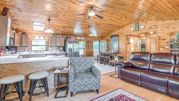 A spacious cabin interior with a wooden ceiling, a central dining area, a leather sofa, and a bar area. - Picturesque Phoenix Vacation Home on Oswego River! (Phoenix)