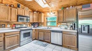 A modern kitchen with wooden cabinets, stainless steel appliances, and a large window. - Picturesque Phoenix Vacation Home on Oswego River! (Phoenix)