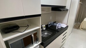A compact kitchen with a microwave, refrigerator, sink, and a small countertop. - Flat Ofurô 09 VP by La Playa (Ipojuca)