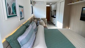 A modern bedroom with a large bed, a small kitchenette, and a bathroom. - Flat Ofurô 09 VP by La Playa (Ipojuca)
