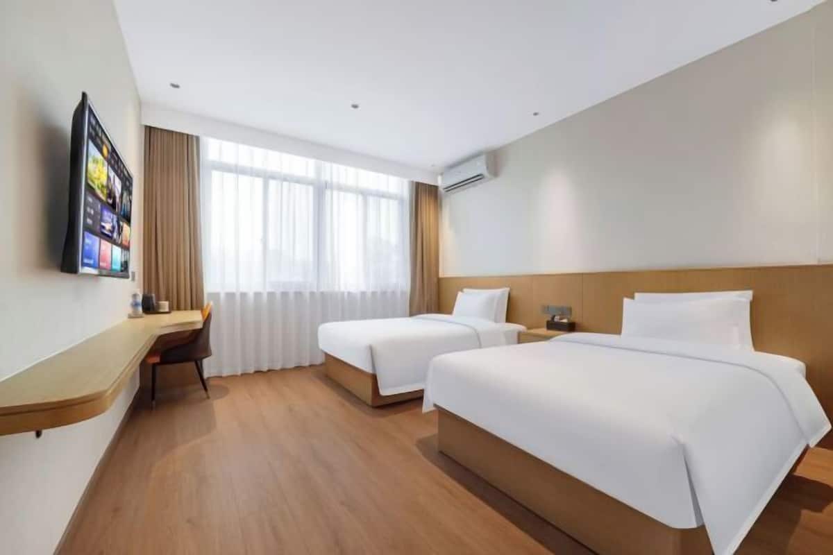 A hotel room with two beds, a desk, a TV, and a large window.