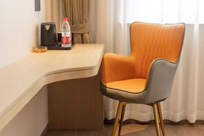 A modern hotel room with a curved wooden desk, a single orange and gray upholstered chair with gold legs, a bottle of water, a red can, and a black object on the desk.
