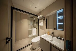 A modern bathroom with a glass-enclosed shower, a white toilet, a sink with a mirror, and a towel rack.