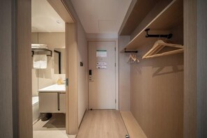 A narrow hallway with a wooden wardrobe on the right, a door at the end, and a bathroom visible on the left.