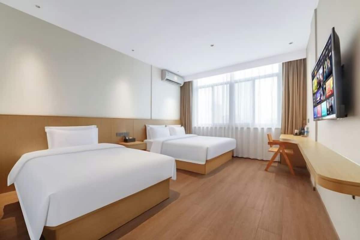 A hotel room with two beds, a desk, a chair, a TV, and a large window with curtains.