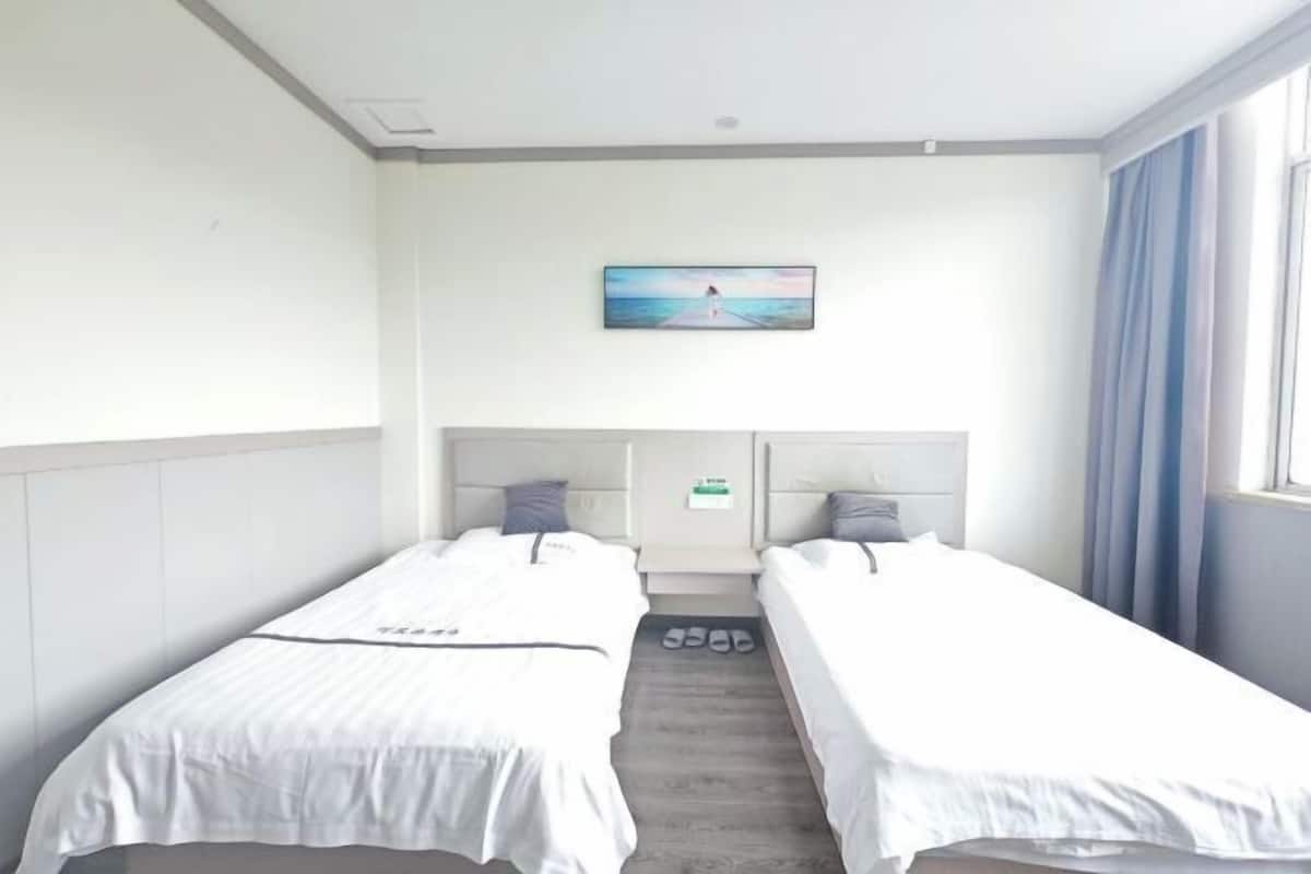A hotel room with two single beds, a painting on the wall, and a window with curtains.