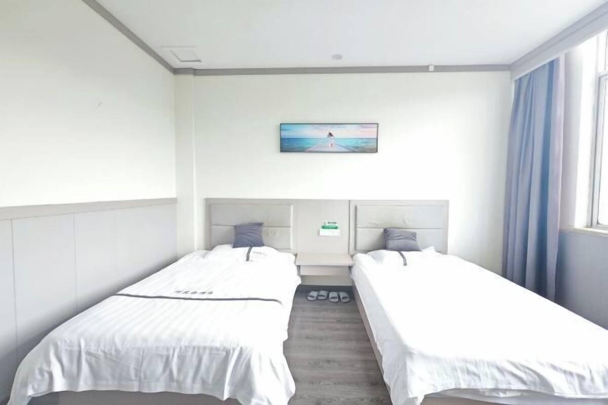A hotel room with two single beds, a painting on the wall, and a window with curtains.