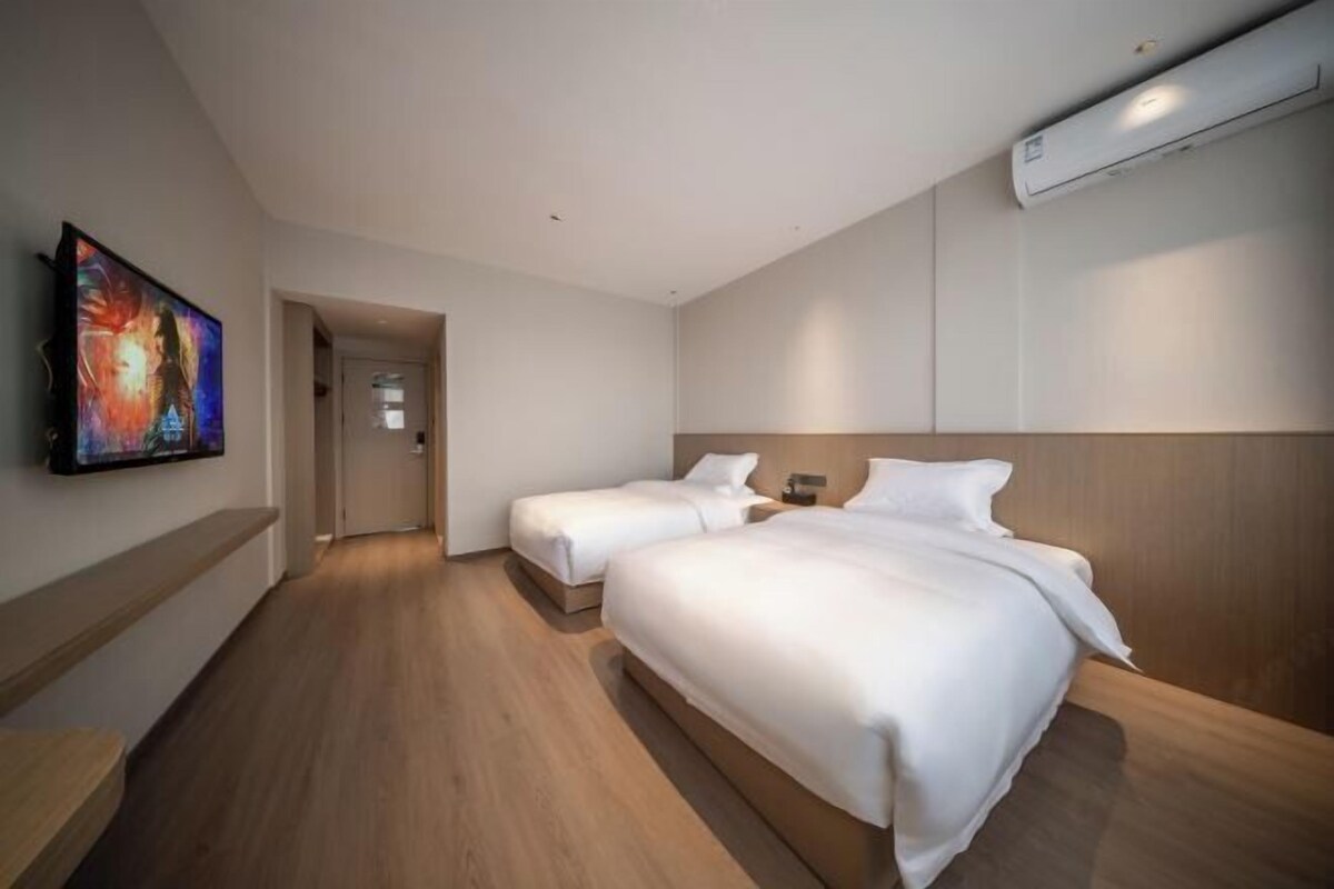 A hotel room with two beds, a painting on the wall, and an air conditioning unit.