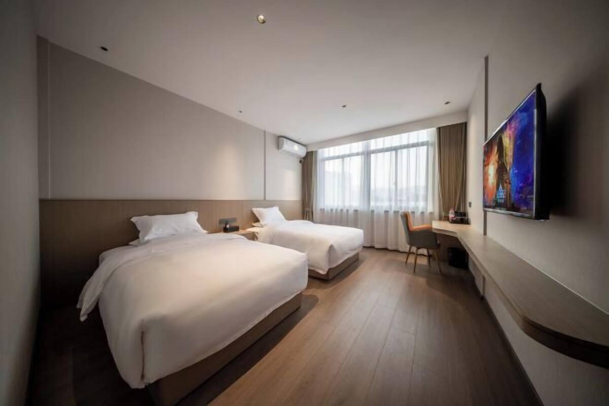 A hotel room with two beds, a desk, a chair, a flat-screen TV, and a large window with curtains.