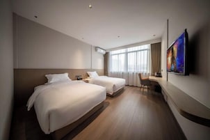 Habitación de hotel con dos camas, un escritorio, una silla, un televisor de pantalla plana y un ventanal grande con cortinas.