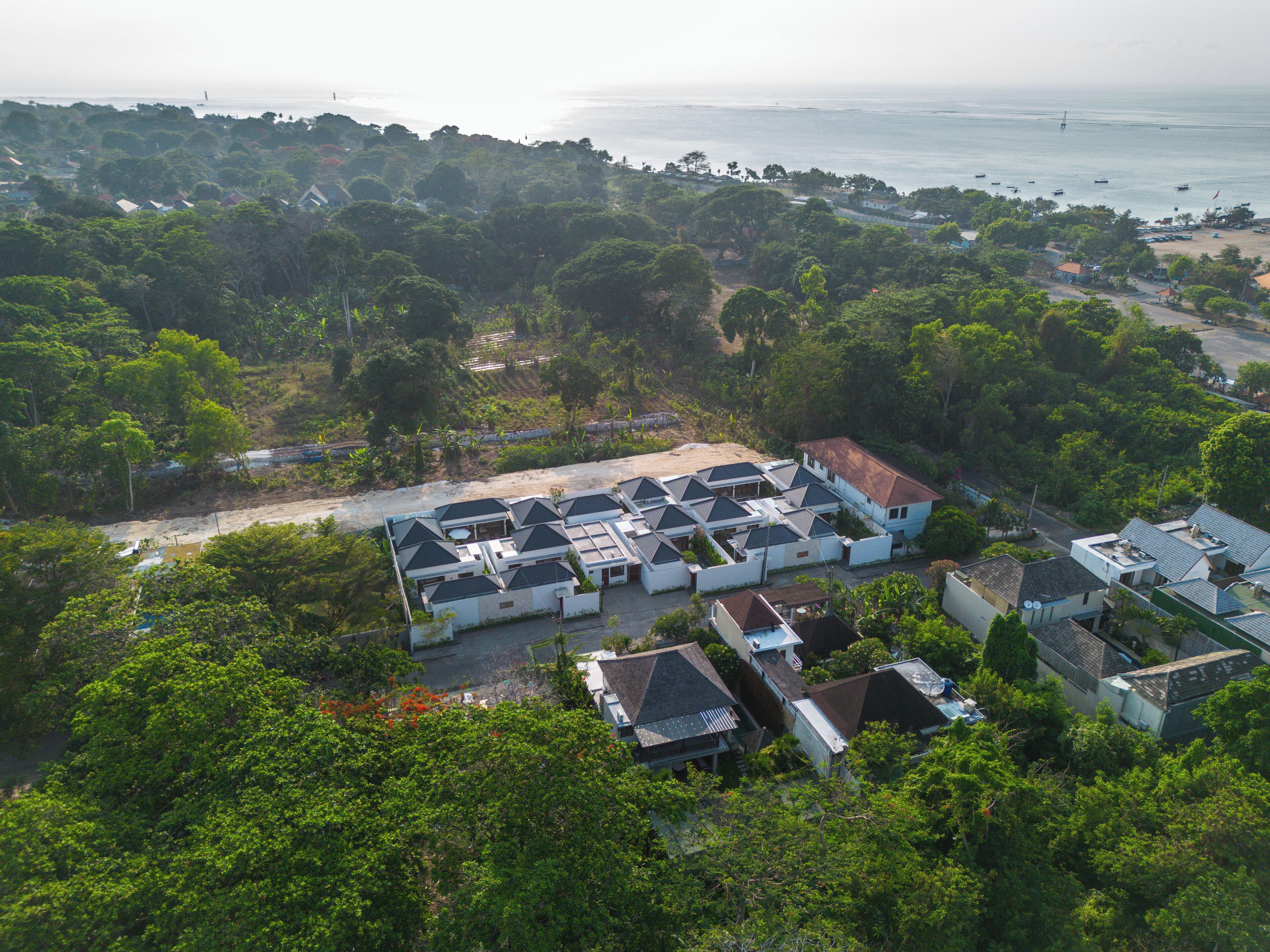 An aerial view of a residential area with houses, a beach, and boats in the distance.
