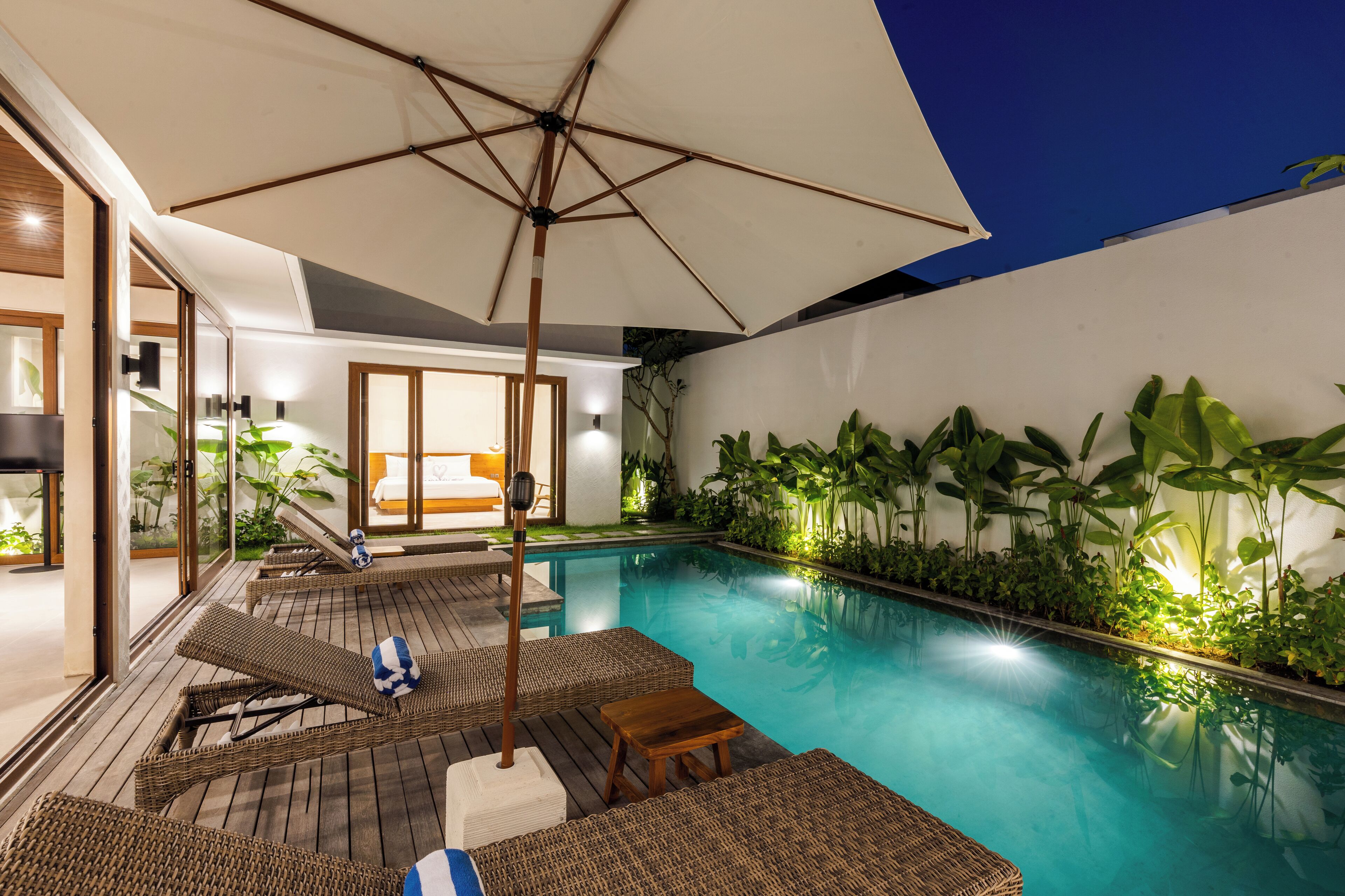 Un espace piscine aménagé avec des fauteuils de relaxation en osier, une table en bois et un parasol.