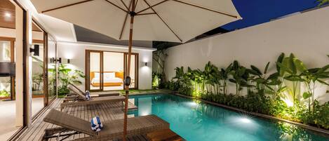 A pool area with wicker lounge chairs, a wooden table, and an umbrella.