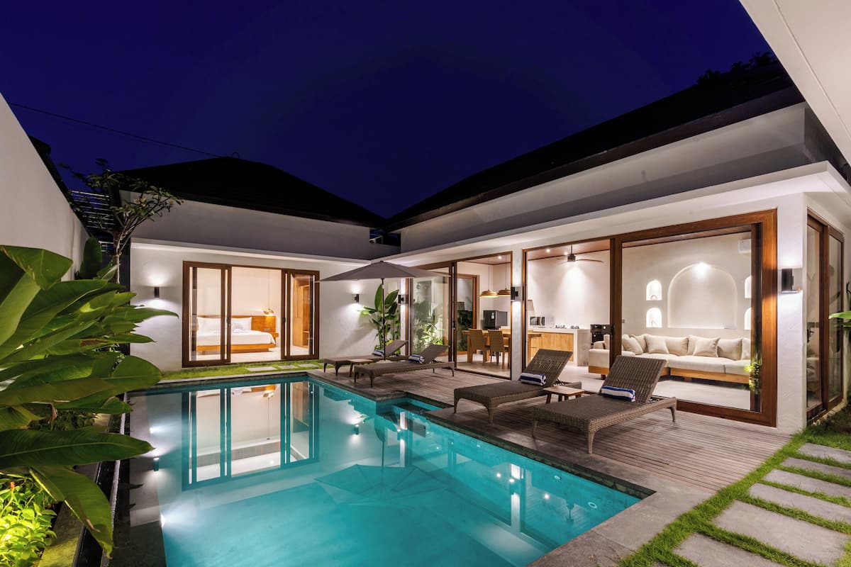 Ein modernes Haus mit Swimmingpool, Gartenmöbeln und einem gut beleuchteten Innenraum.