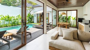A modern living room with a sofa, a dining table, and a pool area visible through large glass doors. - J4 Villas Sanur (Denpasar)