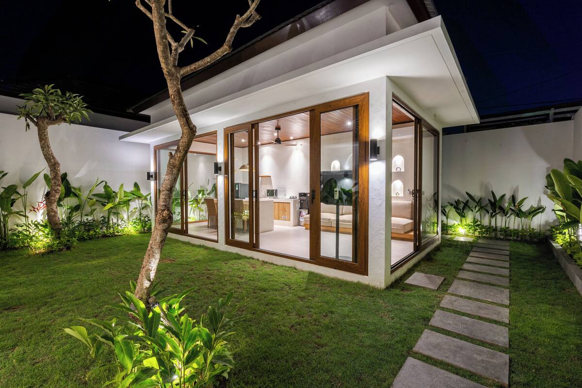 Ein modernes Haus mit einem verglasten Wohnbereich, einer sichtbaren Küche und einem gepflegten Rasen.
