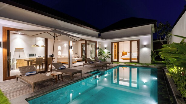 A modern outdoor pool area with lounge chairs, a wooden deck, and a glass-enclosed living space. - J4 Villas Sanur (Denpasar)