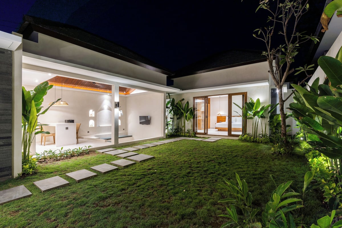 Ein modernes Haus mit gepflegtem Rasen, einer Terrassenanlage und einem einsehbaren Innenraum mit Essbereich und Küche.