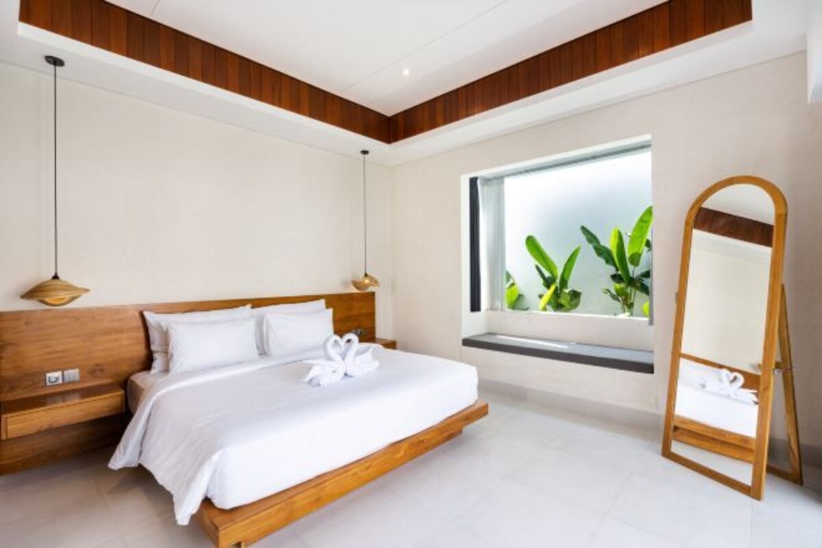 Une chambre moderne avec un lit en bois, une grande fenêtre donnant sur un paysage verdoyant et un miroir à cadre en bois.