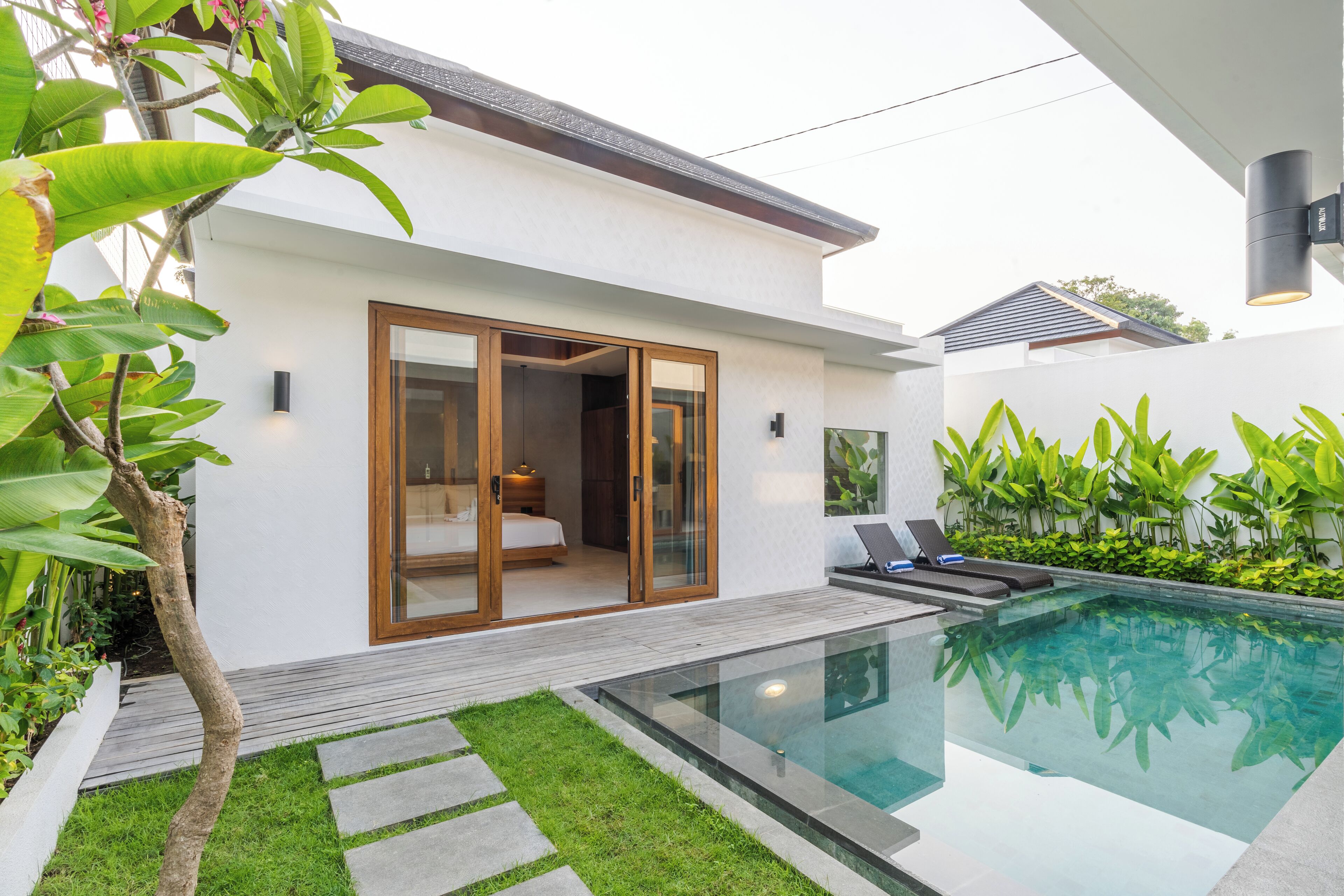 A modern house with a glass door leading to a bedroom, a swimming pool, and a well-maintained garden.