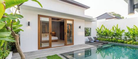 A modern house with a glass door leading to a bedroom, a swimming pool, and a well-maintained garden.
