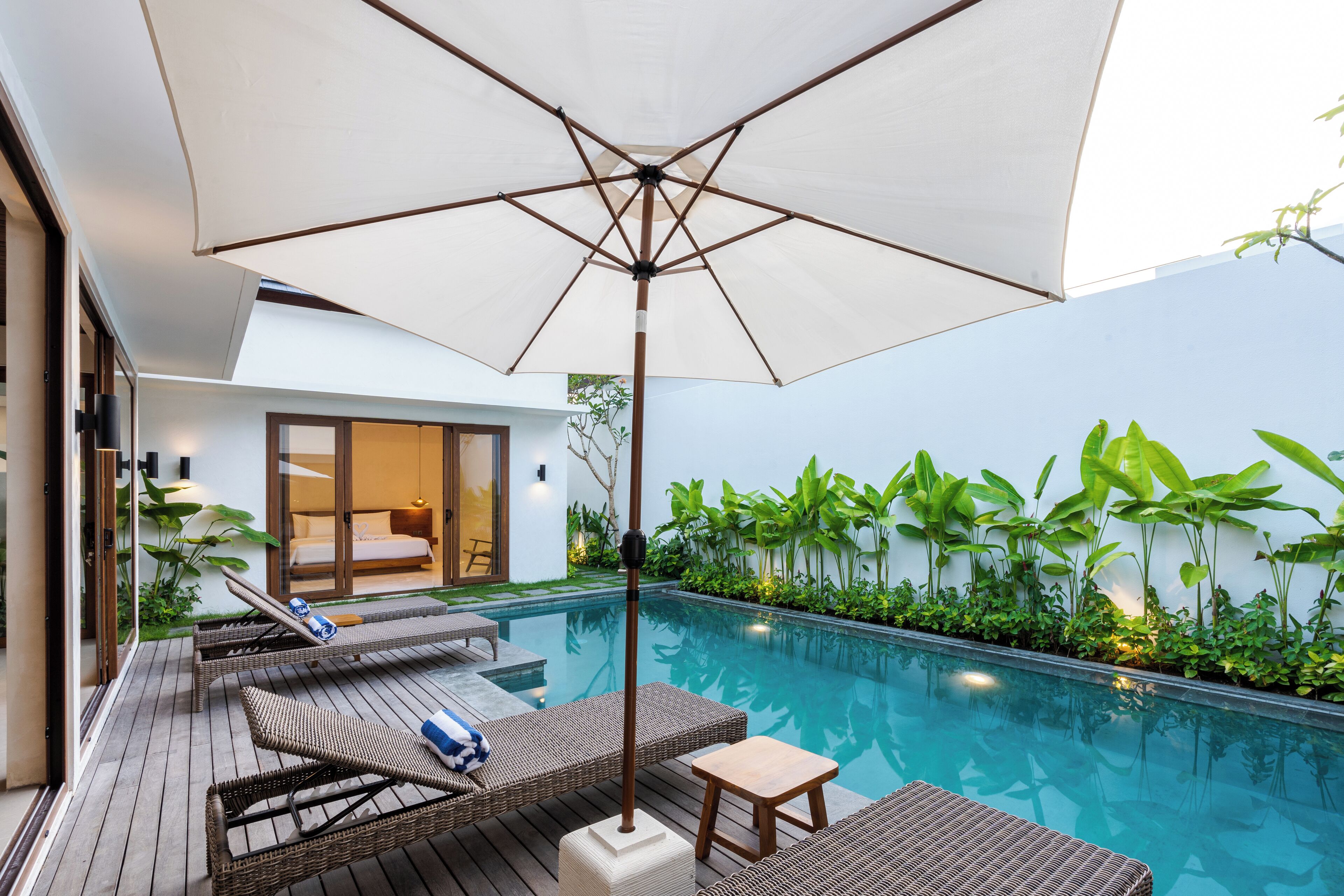 A modern outdoor pool area with wicker loungers, a small table, and a large umbrella.