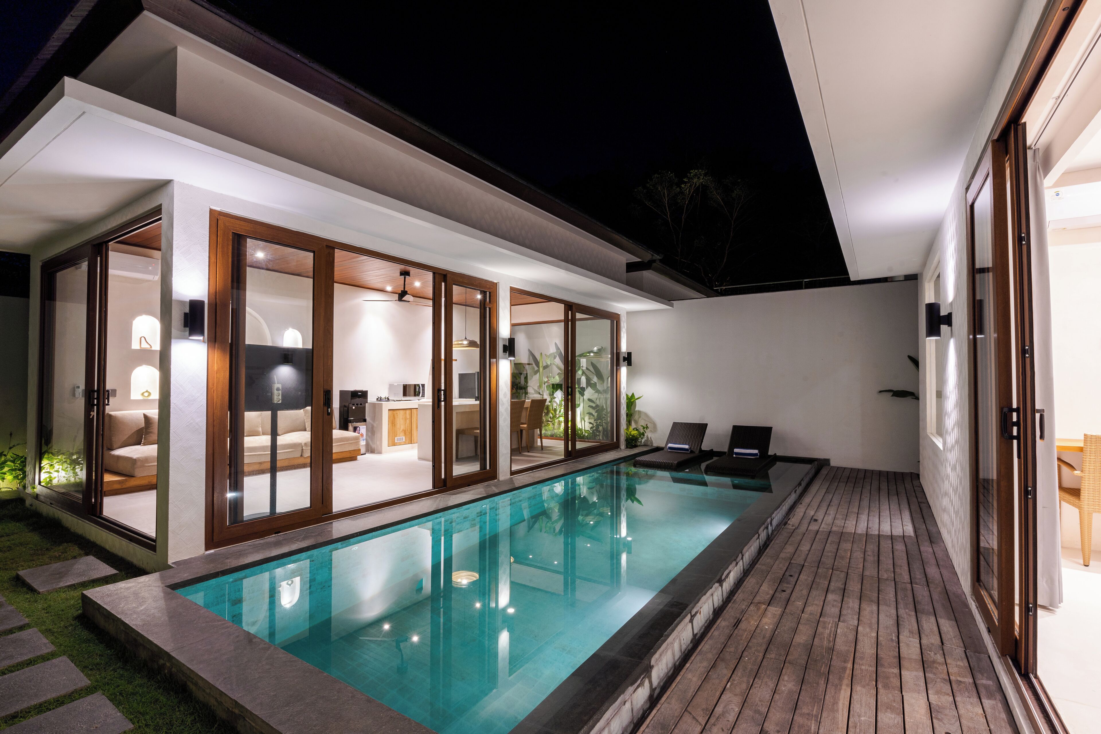 A modern house with a swimming pool, glass doors leading to a living area, and a wooden deck.
