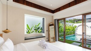 A modern hotel room with a large bed, a window with plants, a pool view, and a sliding glass door. - J4 Villas Sanur (Denpasar)