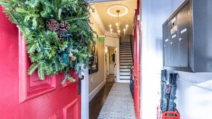 A hallway with a red door, a Christmas wreath, a chandelier, a staircase, and a metal cabinet.
