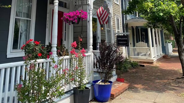A traditional house with a porch, potted plants, and a sign for Long & Foster Realty.