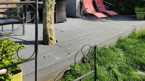 Eine Terrasse mit einem kleinen Gartenhaus, zwei roten Liegestühlen und einem Baum.