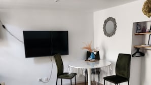 Ein Essbereich mit einem runden Tisch, zwei Stühlen, einem an der Wand montierten Fernseher und einem Regal mit Gegenständen.