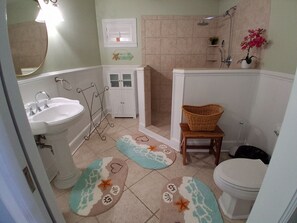 A bathroom with a sink, mirror, shower, toilet, and decorative rugs. - Ochlocknee Bay Waterfront King Suite Private Dock Top Floor (Panacea)