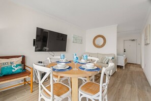 Un comedor con una mesa redonda, sillas blancas y un televisor montado en la pared.