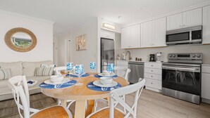 Une cuisine moderne avec des meubles blancs, des appareils en acier inoxydable et un coin repas comprenant une table ronde et des chaises blanches.