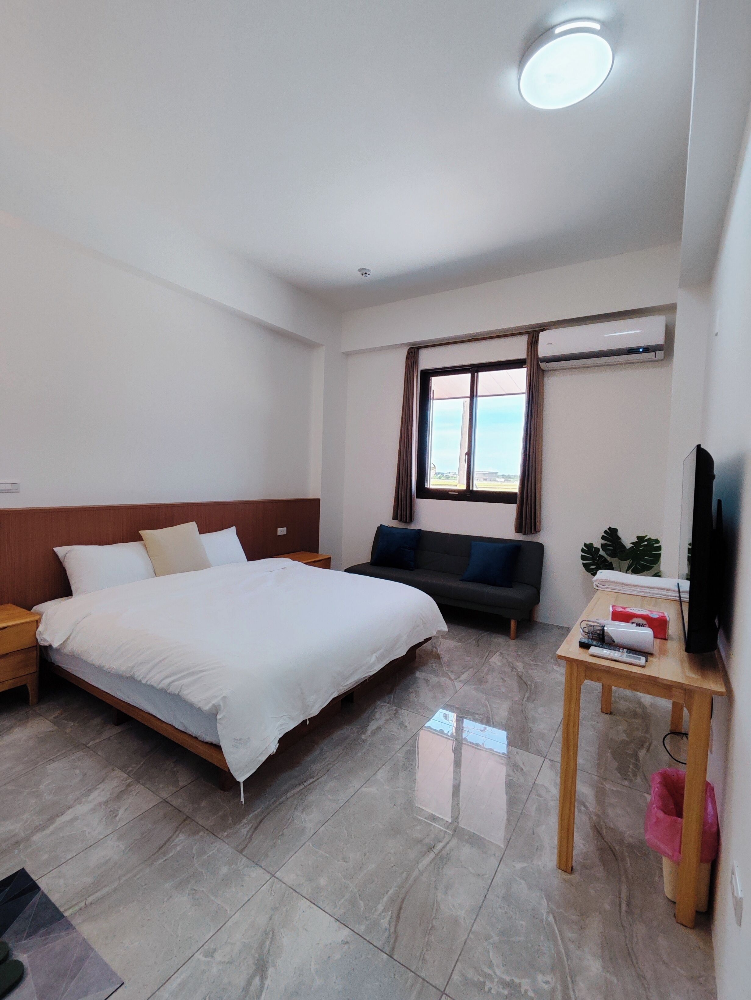 A hotel room with a bed, a sofa, a TV, and a window with curtains.
