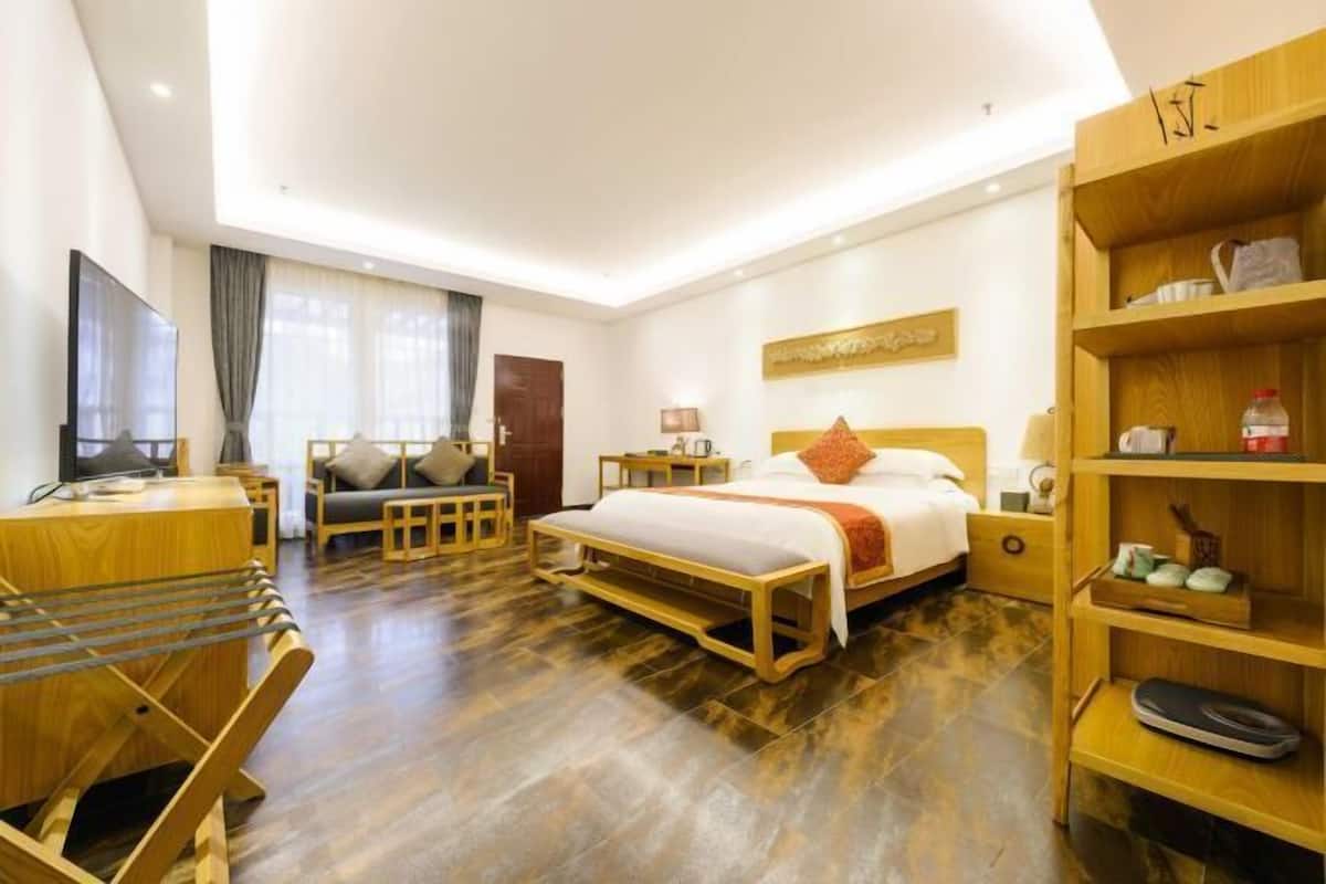 Une chambre d’hôtel moderne équipée d’un lit, d’un bureau, d’une chaise, d’un téléviseur et d’une étagère en bois où sont posés divers objets.