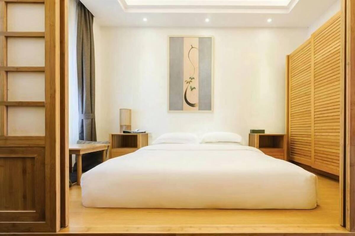 Une chambre à coucher bien aménagée, avec un grand lit, une table de chevet, une lampe et une œuvre d’art accrochée au mur.