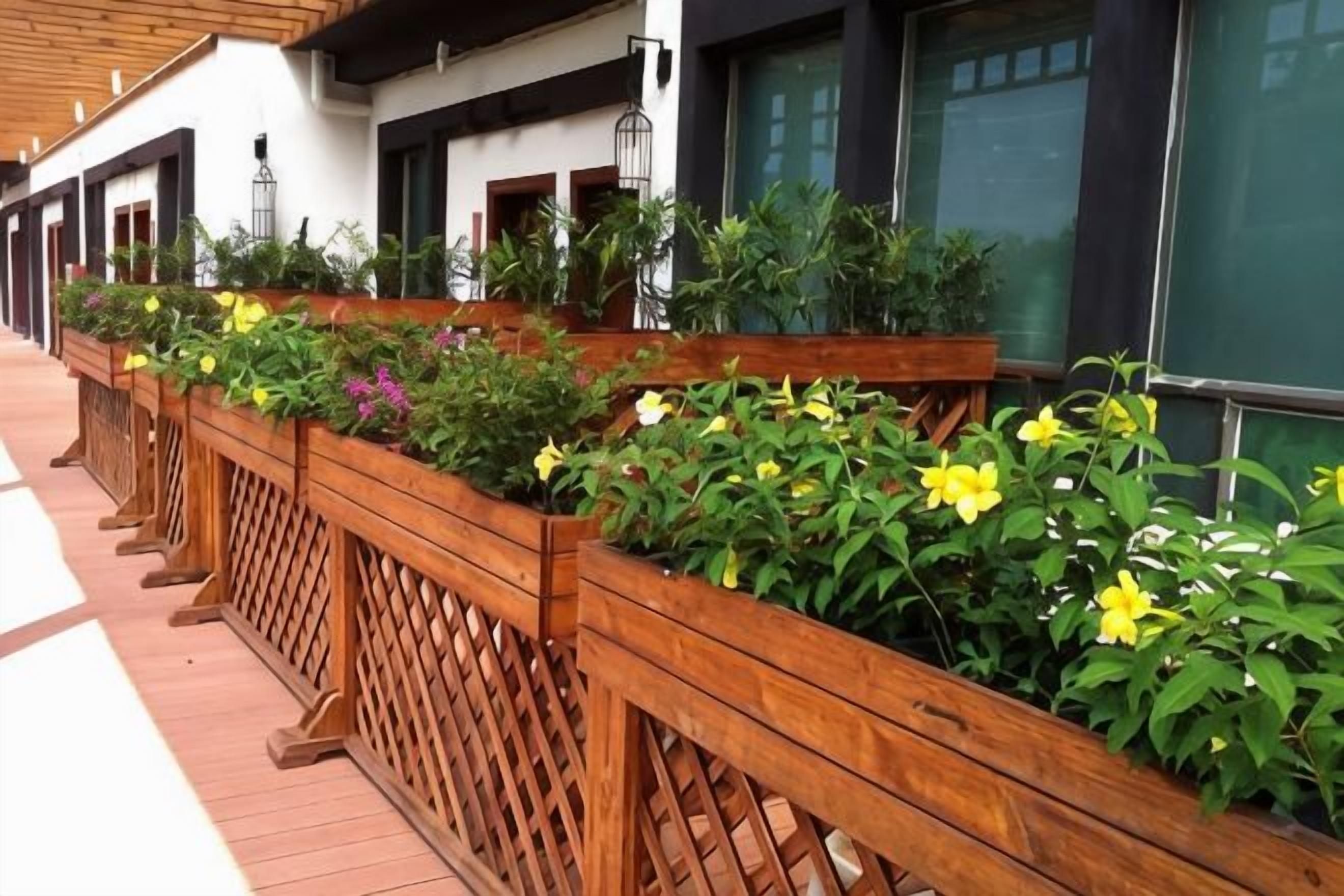 A row of wooden planters with various plants and flowers along a building's exterior.