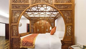 Una cama con dosel adornada con detalles de madera labrada, un cabecero de madera y una mesita de noche con una lámpara.
