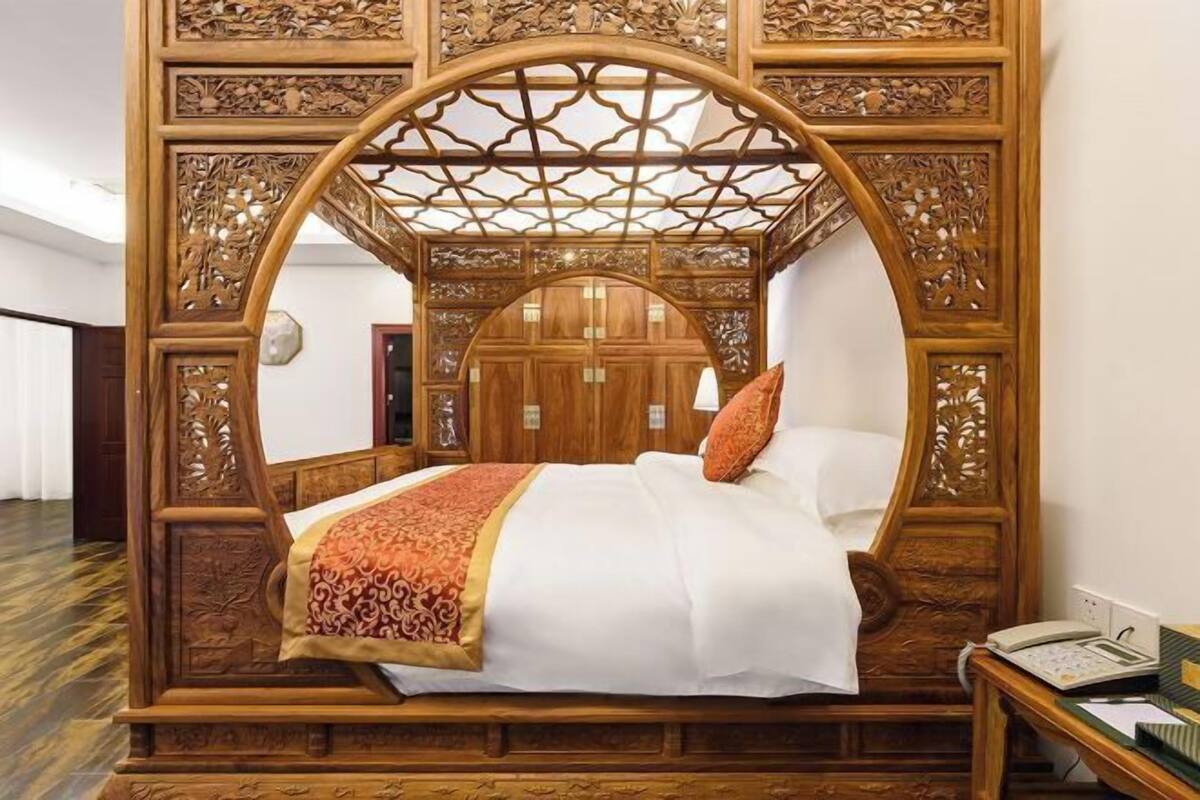 Un lit à baldaquin orné de sculptures complexes, avec une tête de lit en bois et une table de chevet dotée d’une lampe.