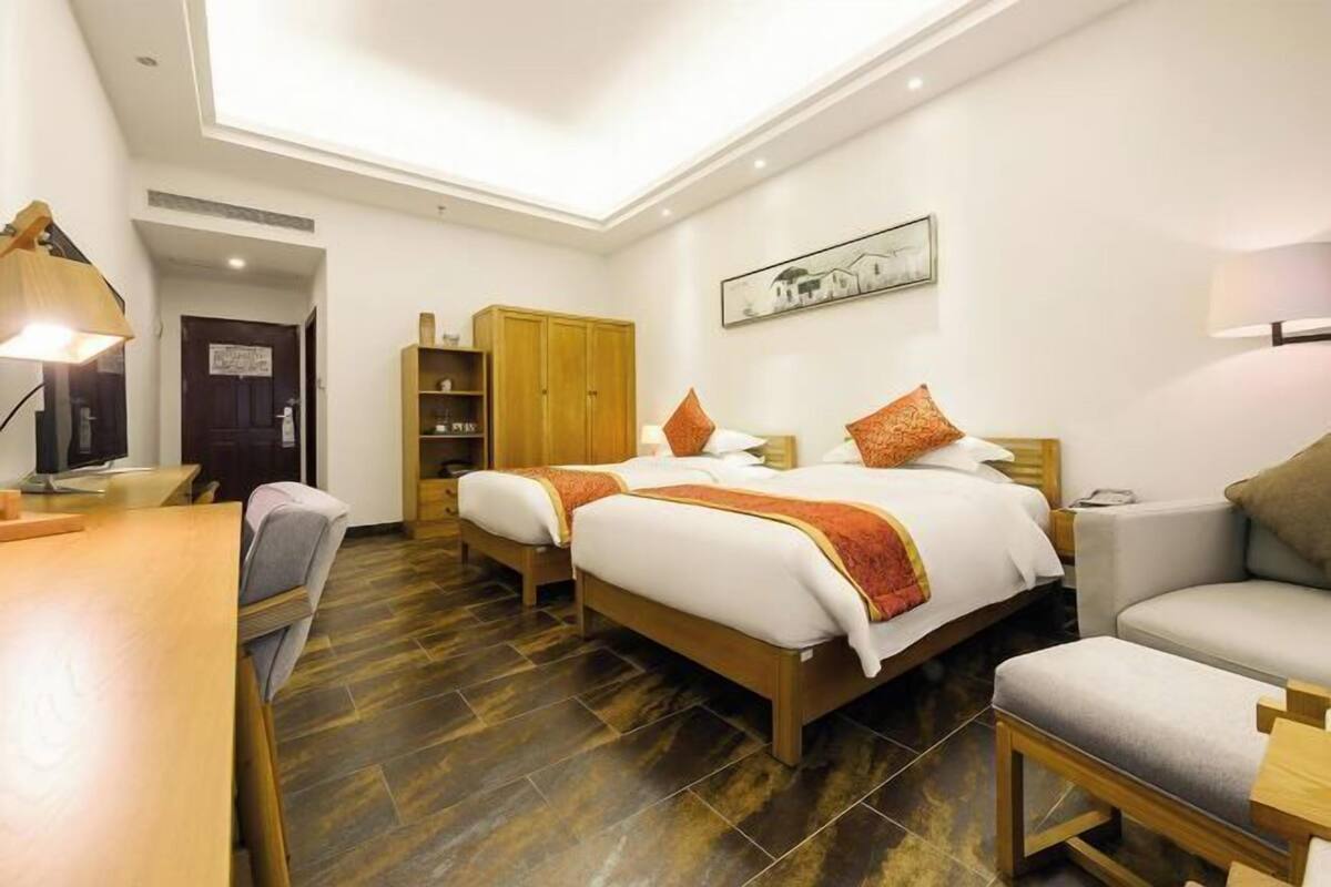 Une chambre d’hôtel avec deux lits, un bureau, une chaise, une armoire et un tableau au mur.